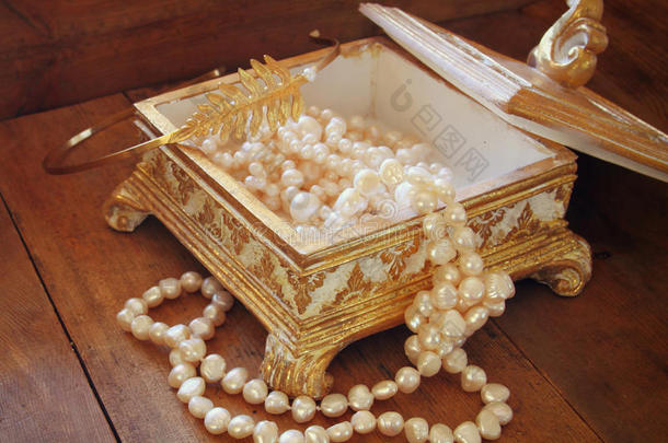 一个美丽的古董黄金珠宝盒，木制桌子上有天然的白色珍珠。 复古过滤图像