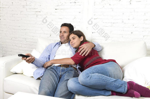 一对相爱的夫妇拥抱在家里的沙发上，放松地看电视上的电影，男人<strong>拿</strong>着<strong>遥控</strong>器