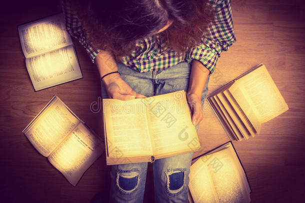 女孩穿着衬衫，拿着一本书，坐在地板上，围绕着她，展开打开的书，特写复古的色调