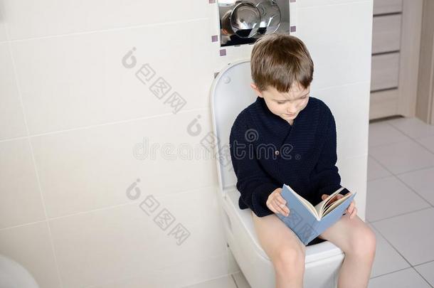 男孩坐在马桶上读一本蓝色的书