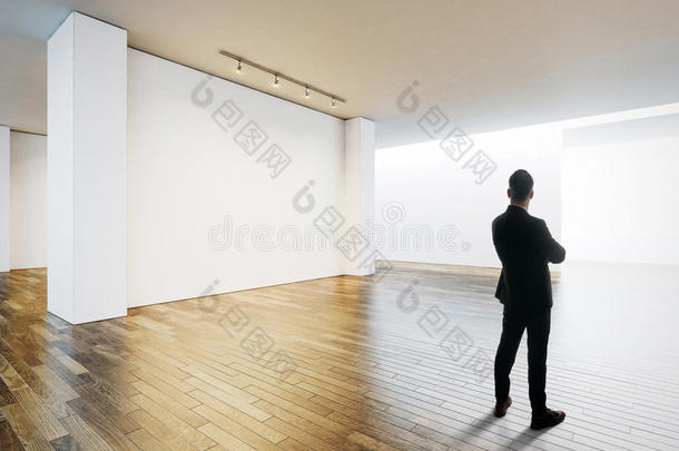 商人站在博物馆内部白色墙壁对面，有木地板。 水平的
