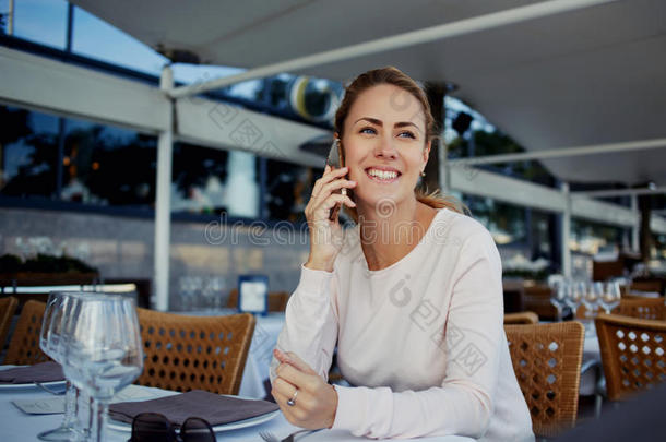 有吸引力的年轻女人在手机上愉快地交谈，同时在舒适的咖啡馆等待她的点菜