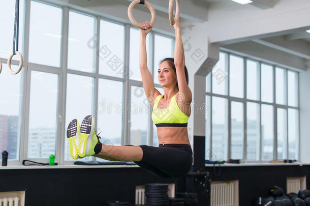 适合的妇女锻炼与体操环抬腿在健身房。