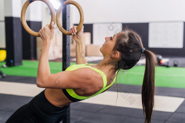 运动员适合妇女在健身房锻炼，拉起体操环侧视图。