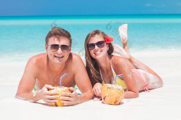 一对戴着太阳镜的夫妇在热带海滩喝椰子汁
