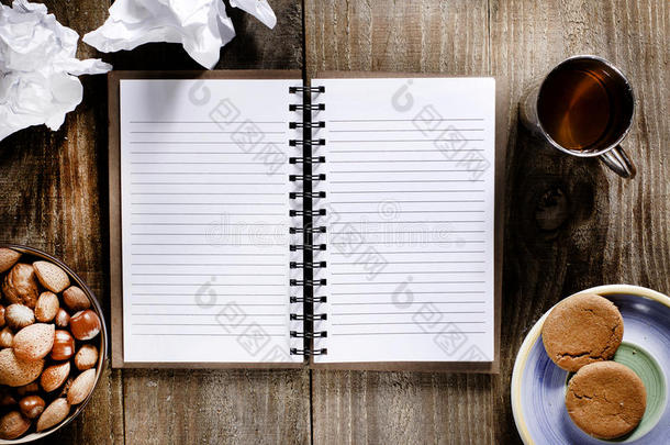 一本打开的笔记本，木桌上有空白页。一杯茶，坚果和饼干零食