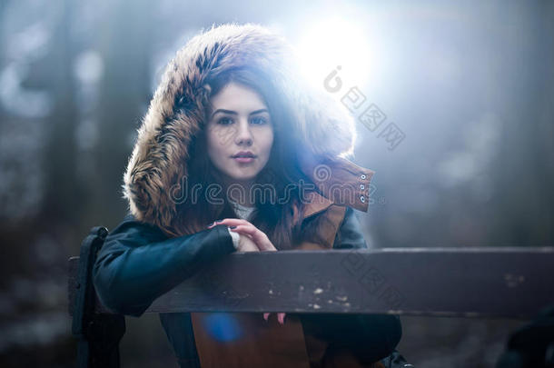 美丽的年轻女孩，棕色毛皮斗篷，享受冬天的风景，坐在公园的长凳上。 十几岁的女孩摆姿势，冬天