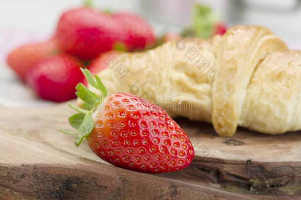 新鲜草莓和新鲜烘焙的黄油牛角面包在木制背景。 摄影棚的照片。