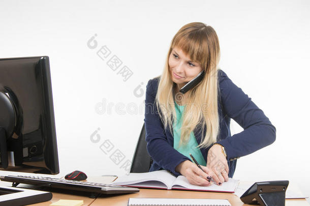 商务妇女在电话里交谈，在办公室的本子上记录信息，看着显示器