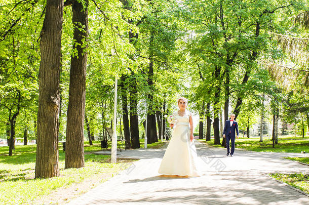 一对穿着婚礼服装的夫妇，手里拿着一束鲜花和绿色植物，在花园的背景下