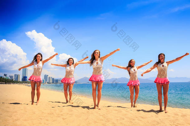 舞蹈中的啦啦队队员在沙滩上摆出双臂背对大海的姿势