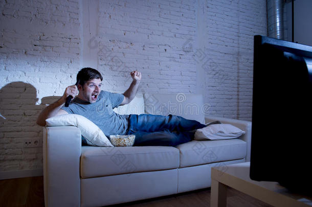 有魅力的男人在家躺在客厅的沙发上看电视上的体育比赛庆祝进球