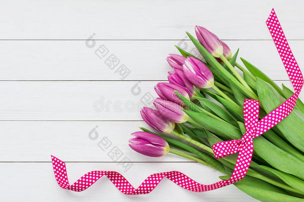 一束明亮的粉红色郁金香，在白色的木制背景上装饰着粉红色的丝带。 上面的风景
