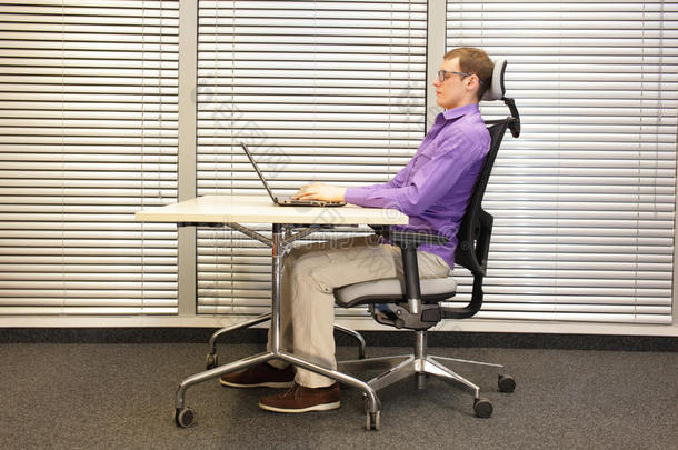 正确的坐姿在工作站。 坐在椅子上的人用笔记本电脑工作