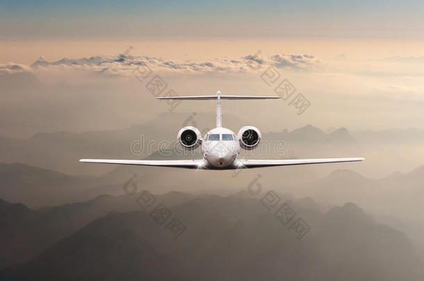 飞机在日落时飞过云层和阿尔卑斯山。 大型客机或货机的正面视图，商务喷气式飞机