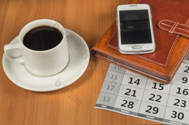 木制桌子上的咖啡、手机、规划师和日历