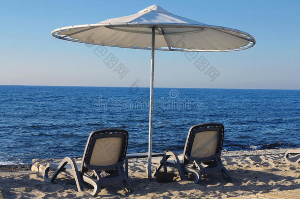 海滩椅子和雨伞在海边的沙滩上，蓝天