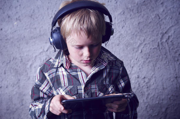 金发男孩听音乐或用耳机看电影，用数字桌子