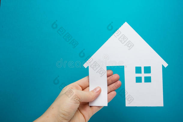 手拿着蓝色背景上的白纸屋人物。 房地产概念。 生态建筑。 复制空间顶部视图。
