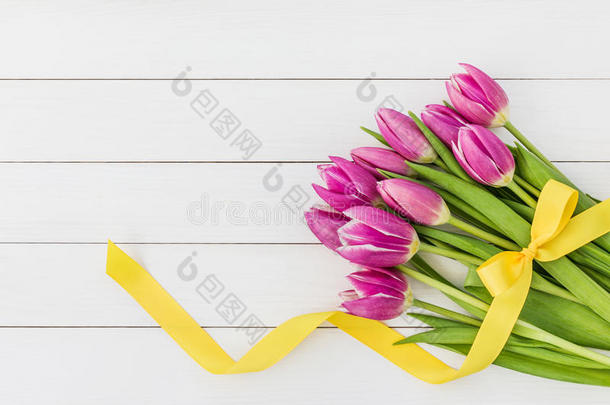 一束明亮的粉红色郁金香，在白色的木制背景上装饰着黄色的丝带