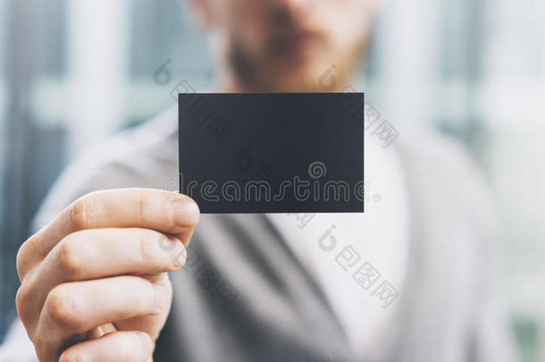 特写照片男子穿着休闲衬衫，显示空白黑色名片。 模糊的背景。 准备好了