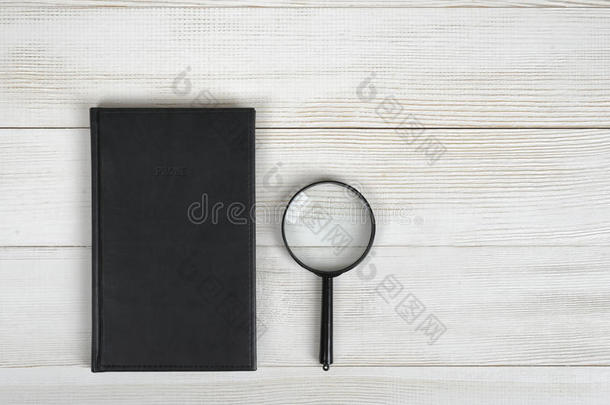 黑色笔记本和放大镜平放在轻木表面。