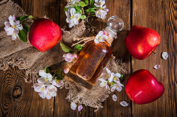 一瓶苹果醋（苹果醋），新鲜苹果和苹果树花在木制背景上。