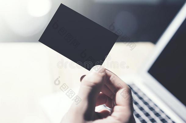 特写图像男子显示空白的黑色名片，并使用现代笔记本电脑在木桌上模糊的背景。 模拟