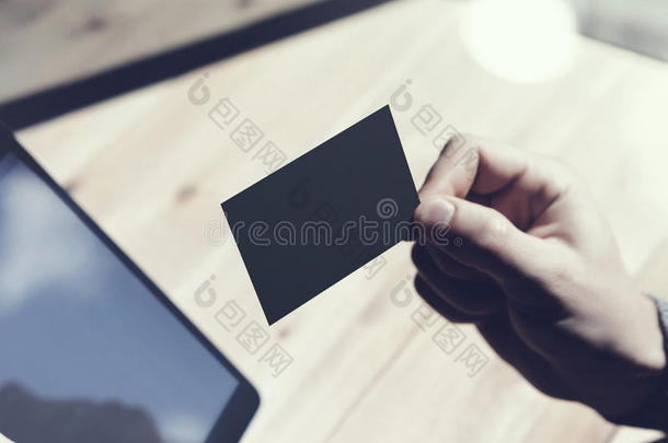 特写男子显示空白的黑色名片，手持现代数字平板电脑。木桌模糊背景