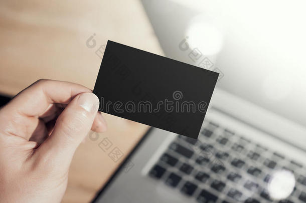 特写照片男子显示空白黑色名片和使用现代笔记本电脑。木桌模糊背景。 模型准备好了