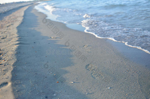 湿沙上的脚印，日落时在宁静的海滩上的波浪。 蒂