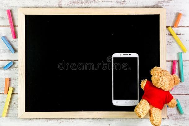 空白<strong>黑板</strong>，泰迪熊和智能手机在木桌上。<strong>模板</strong>模拟添加您的设计，并留下空间旁边的框架