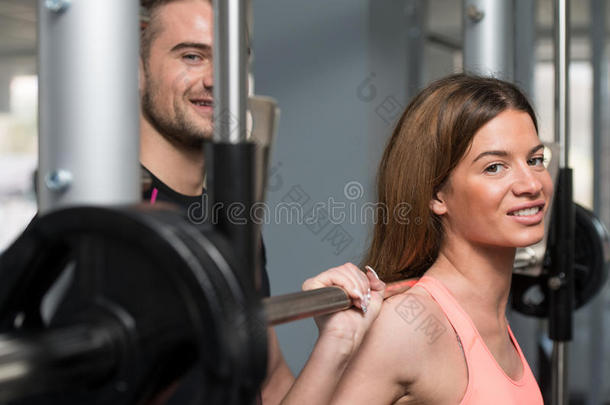 健身房教练帮助女人上杠铃蹲