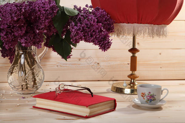 一束紫丁香，书，眼镜，一杯茶和台灯