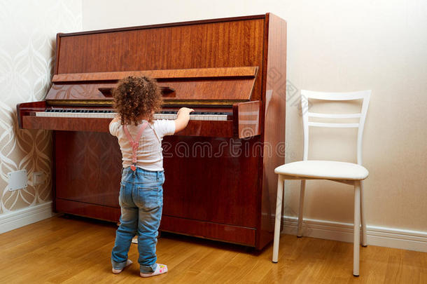 后视图。 一个孩子站在钢琴前演奏旋律。 小钢琴家学会弹钢琴。 宝贝，孩子