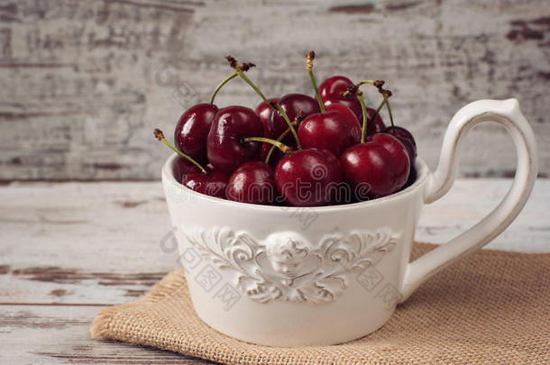一大杯咖啡在前面的天使，白色的碗充满新鲜的樱桃，水果。 轻盈的乡村背景，破旧别致，复古