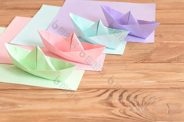 木制桌子上有四只彩色折纸船玩具。 正方形的彩色纸。 暑假创意纸工艺品创意