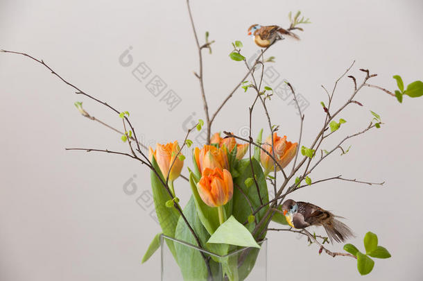 新鲜的春天，一束橙色的郁金香和绿叶，两只小鸟放在漂亮的玻璃花瓶里。 春天的家居时尚装饰