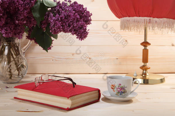 一束紫丁香，书，眼镜，一杯茶和台灯