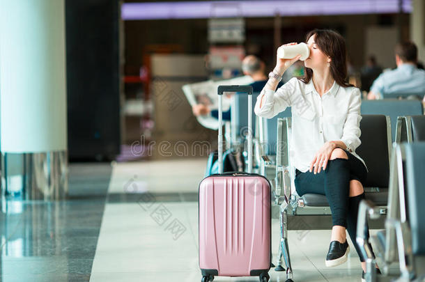 航空公司的旅客在机场休息室里喝咖啡，等待飞机起飞。白种女人拿着玻璃如果