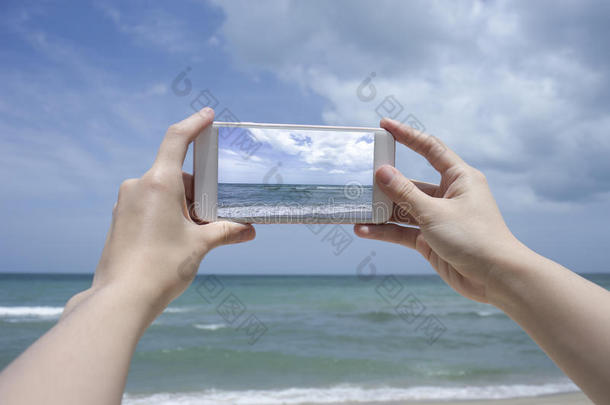 特写女人的手拿着智能<strong>手机</strong>，<strong>手机</strong>，智能<strong>手机</strong>在模糊美丽的蓝海上拍一张大海的照片
