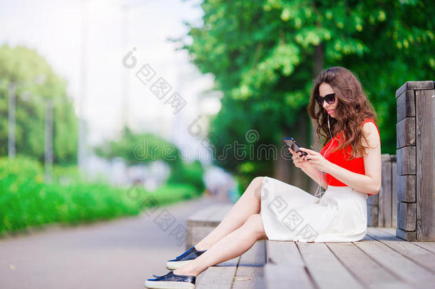 美丽的女孩在暑假用智能手机听音乐。 年轻有吸引力的游客，在户外使用手机