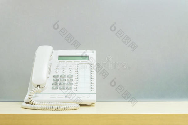 特写白色电话，办公室电话在模糊的木桌和磨砂玻璃墙纹理背景在工作办公室