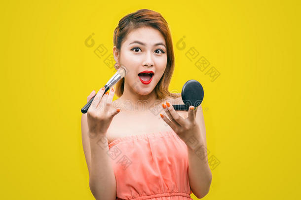 美丽的年轻亚洲女人，镜子在脸颊上涂上粉末