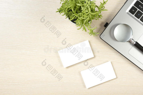 名片空白，笔记本电脑，鲜花和放大镜在办公桌上俯视。企业文具品牌