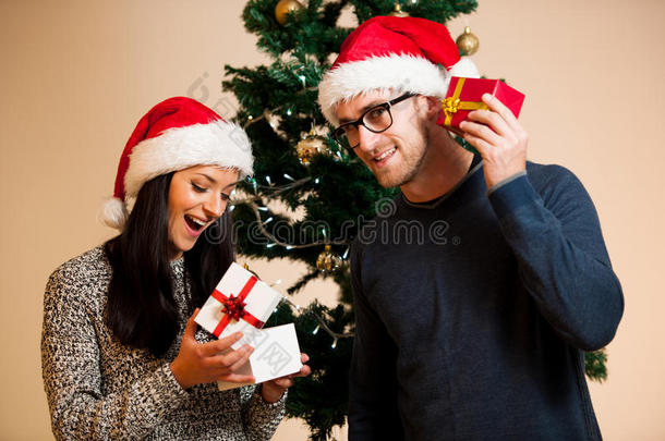 一对年轻的夫妇站在圣诞树前送礼物