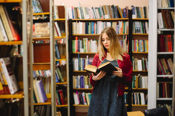 女学生在大学图书馆的书架之间读一本书