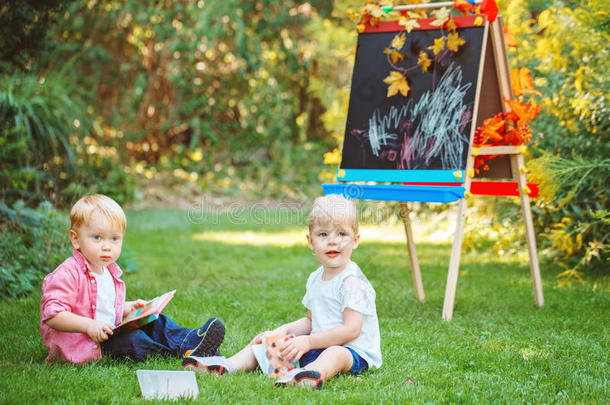 一群两个白人白种人蹒跚学步的孩子，孩子们，<strong>男孩</strong>和女孩，坐在夏天的秋天公园外面，<strong>画画</strong>画架