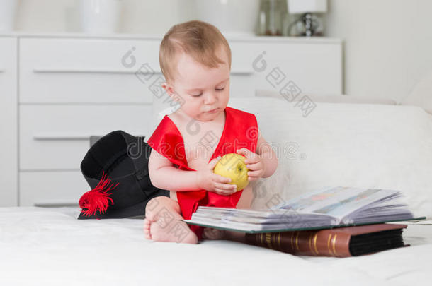 宝贝戴着<strong>毕业</strong>帽和丝带，拿着苹果，读着大书