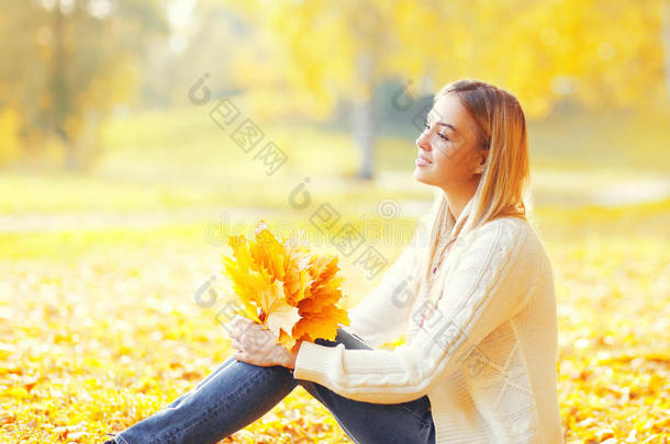 美丽的年轻女人坐在温暖枫叶在温暖的阳光明媚的秋天